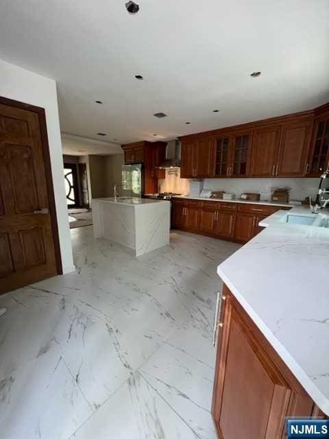 kitchen featuring light stone counters, wall chimney exhaust hood, and sink