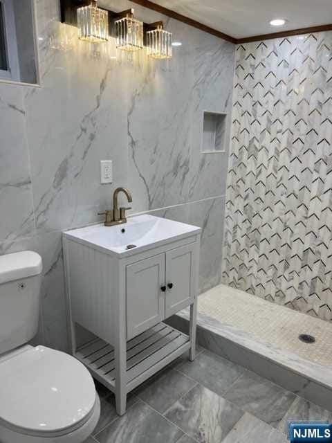 bathroom with a shower, crown molding, vanity, and tile walls