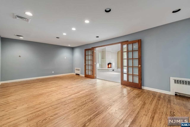 empty room with light hardwood / wood-style flooring, radiator, and french doors