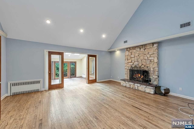 unfurnished living room featuring french doors, high vaulted ceiling, radiator heating unit, light hardwood / wood-style floors, and a stone fireplace