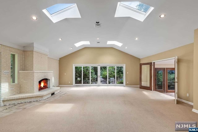 unfurnished living room featuring vaulted ceiling with skylight, carpet floors, and a brick fireplace