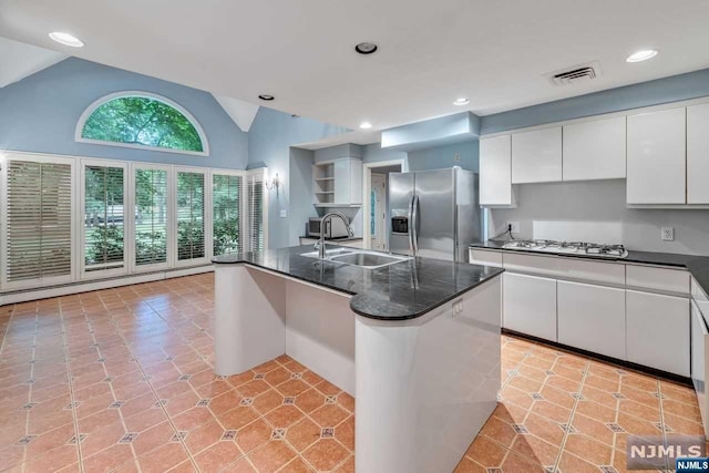 kitchen with stainless steel appliances, vaulted ceiling, sink, white cabinetry, and an island with sink