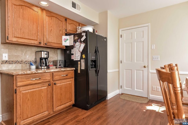 kitchen featuring decorative backsplash, dark hardwood / wood-style flooring, light stone countertops, and black refrigerator with ice dispenser