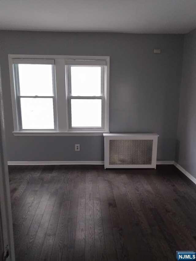 unfurnished room featuring dark hardwood / wood-style floors and radiator heating unit