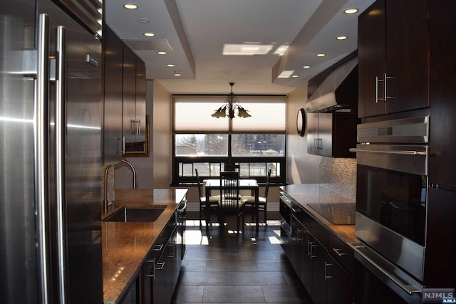 kitchen with sink, stainless steel appliances, range hood, a notable chandelier, and decorative light fixtures