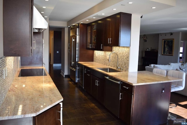 kitchen featuring dishwasher, sink, decorative backsplash, light stone countertops, and a breakfast bar area