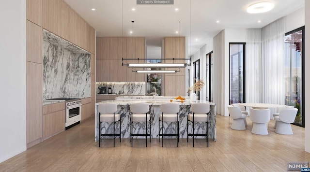 kitchen with high end range, a large island with sink, light hardwood / wood-style flooring, and light stone counters