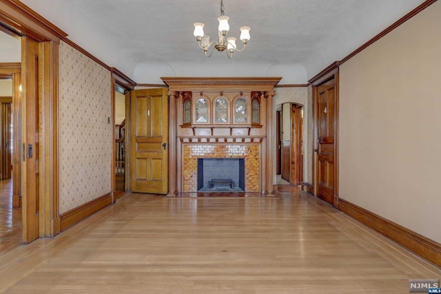 unfurnished living room with crown molding, a fireplace, light hardwood / wood-style floors, and an inviting chandelier