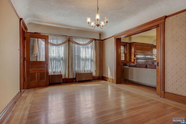 spare room featuring an inviting chandelier, radiator heating unit, a textured ceiling, and light hardwood / wood-style flooring