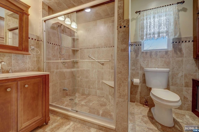 bathroom featuring vanity, toilet, tile walls, and a shower with shower door