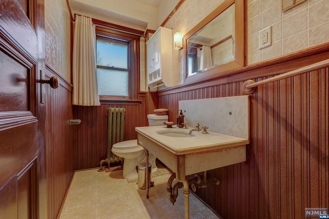 bathroom with toilet, radiator, wood walls, and sink