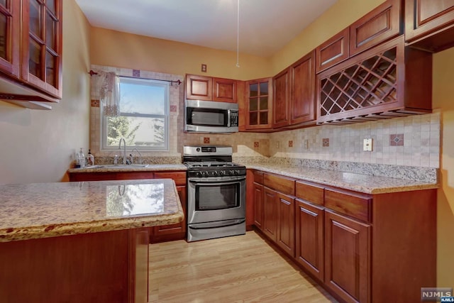 kitchen with light stone countertops, tasteful backsplash, stainless steel appliances, sink, and light hardwood / wood-style flooring