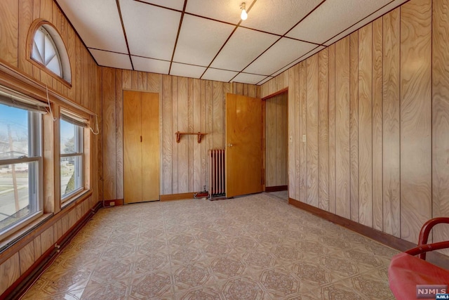 spare room with a drop ceiling, radiator, and wooden walls