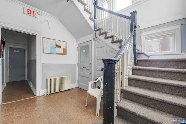 staircase with parquet floors, radiator, and vaulted ceiling