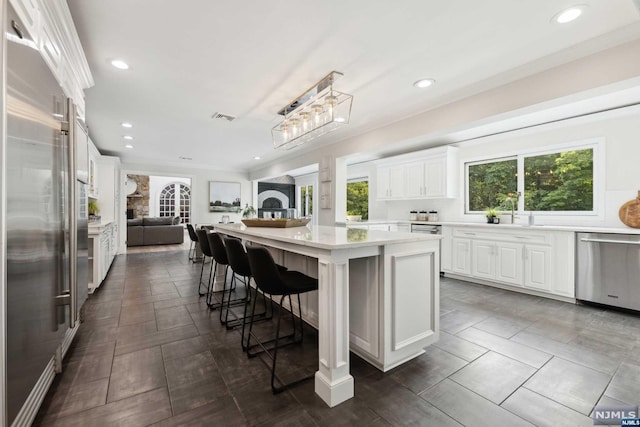 kitchen with a center island, stainless steel appliances, a kitchen breakfast bar, decorative light fixtures, and white cabinets