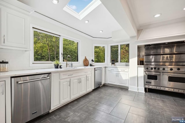 kitchen featuring a skylight, white cabinetry, sink, stainless steel appliances, and decorative backsplash