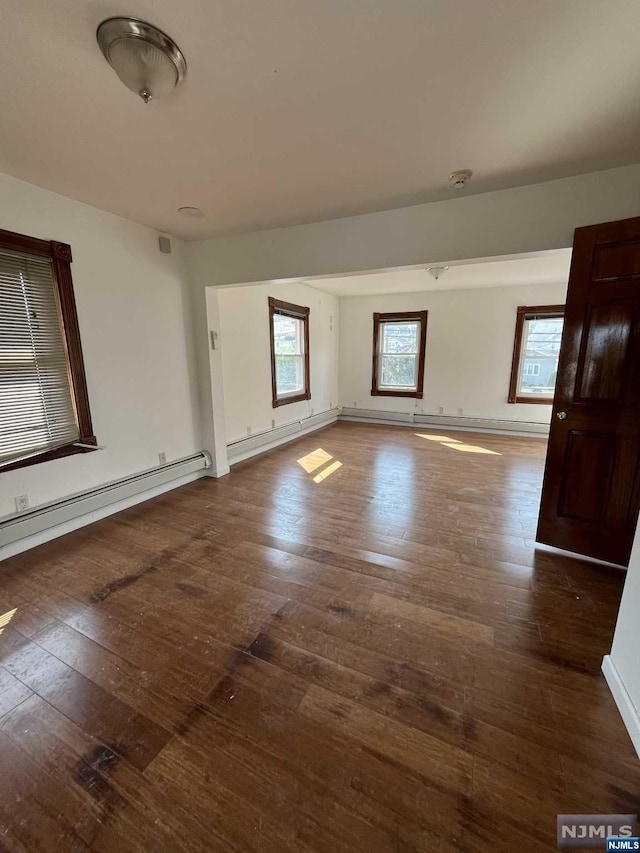 spare room featuring dark hardwood / wood-style flooring, a baseboard radiator, and a healthy amount of sunlight