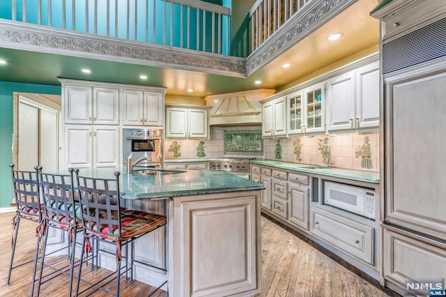 kitchen featuring a high ceiling, a center island with sink, sink, light hardwood / wood-style floors, and stainless steel appliances