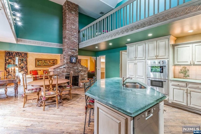 kitchen featuring a center island with sink, sink, a towering ceiling, light hardwood / wood-style floors, and stainless steel appliances