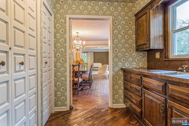 kitchen with sink, dark wood-type flooring, dark brown cabinets, and a notable chandelier