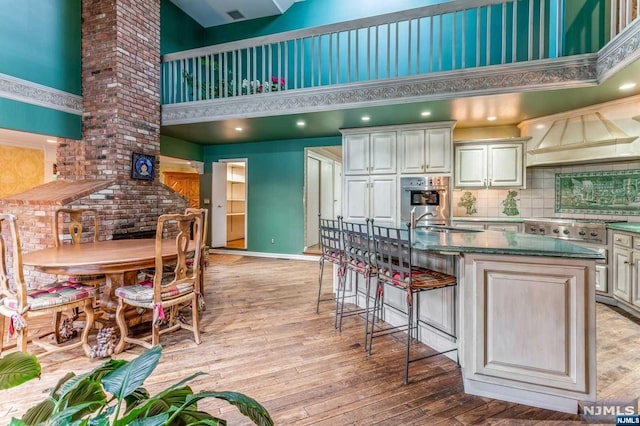 kitchen featuring a high ceiling, light hardwood / wood-style floors, a kitchen island with sink, and premium range hood