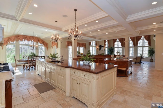 kitchen featuring coffered ceiling, pendant lighting, cream cabinetry, beamed ceiling, and an island with sink