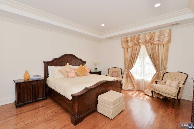 bedroom with wood-type flooring, a raised ceiling, and crown molding