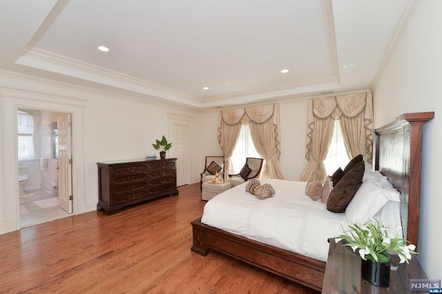 bedroom with hardwood / wood-style floors, ensuite bathroom, crown molding, and a tray ceiling