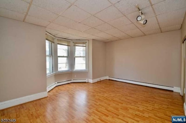 empty room featuring baseboard heating, a paneled ceiling, and wood-type flooring