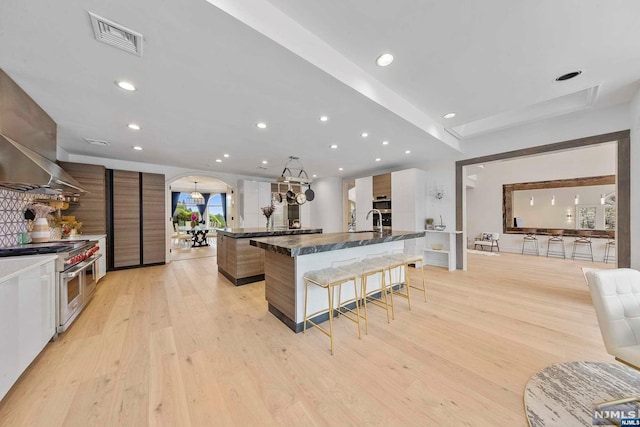 kitchen featuring high end stainless steel range oven, dark stone countertops, a spacious island, light hardwood / wood-style floors, and a breakfast bar area