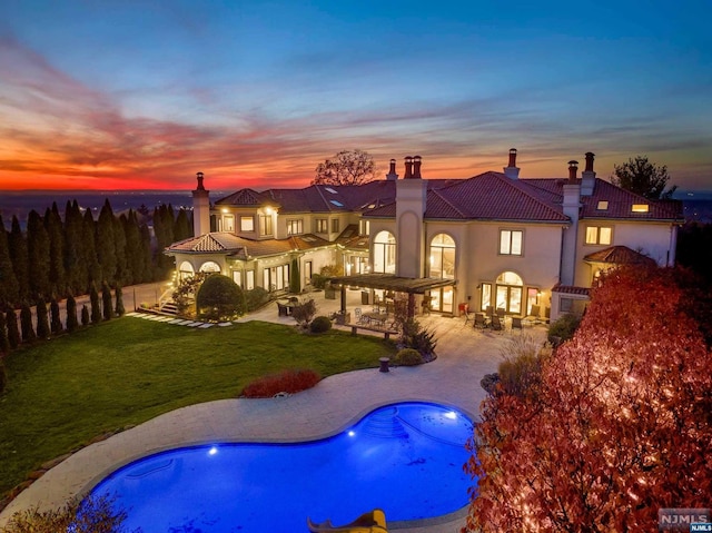 back house at dusk featuring a yard and a patio