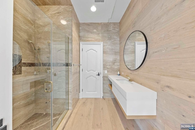 bathroom with vanity, a shower with shower door, tile walls, and hardwood / wood-style flooring