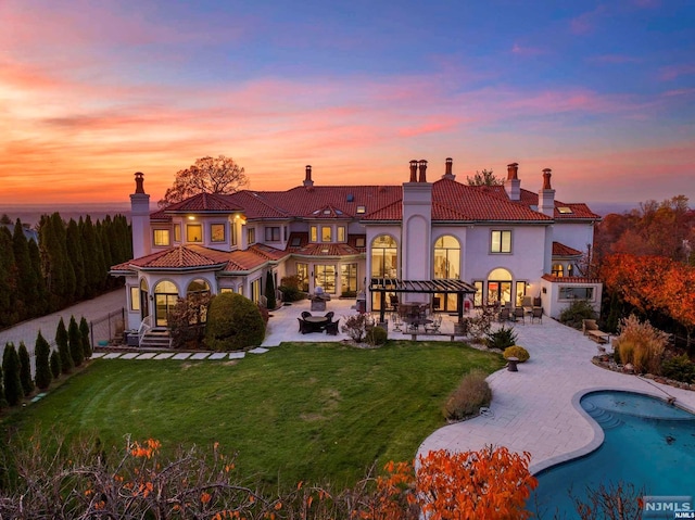 back house at dusk with a lawn and a patio area