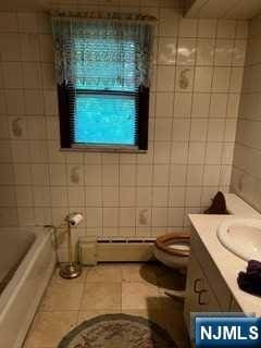 bathroom featuring vanity, tile patterned flooring, toilet, baseboard heating, and tile walls