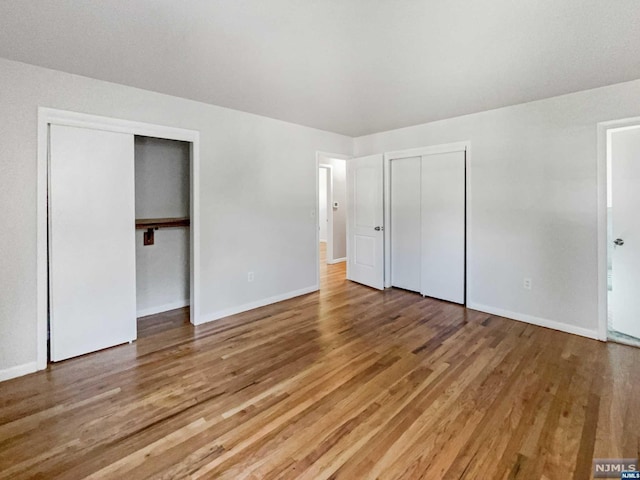 unfurnished bedroom with multiple closets and hardwood / wood-style floors