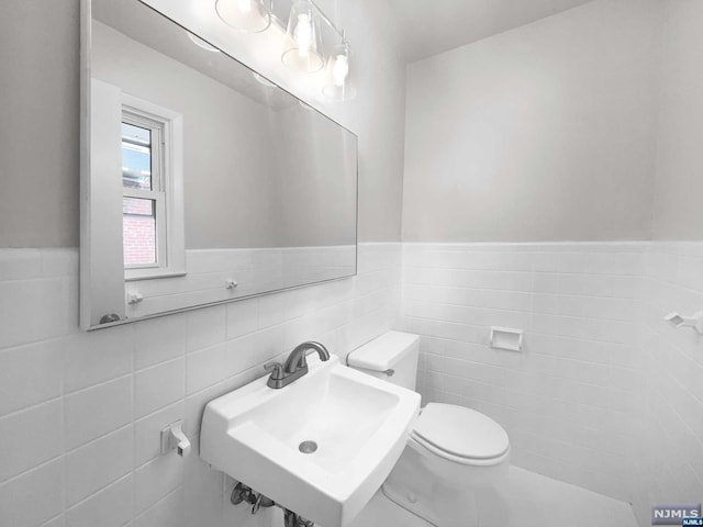 bathroom featuring toilet, tile walls, and sink