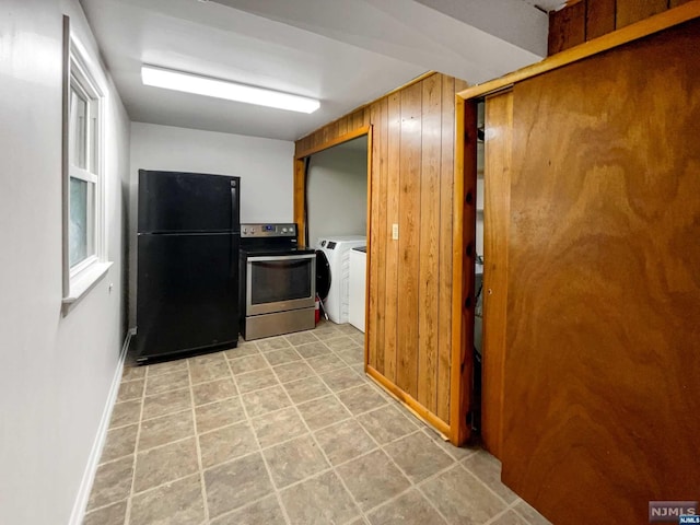 kitchen featuring black fridge, washer and clothes dryer, electric range, and wood walls