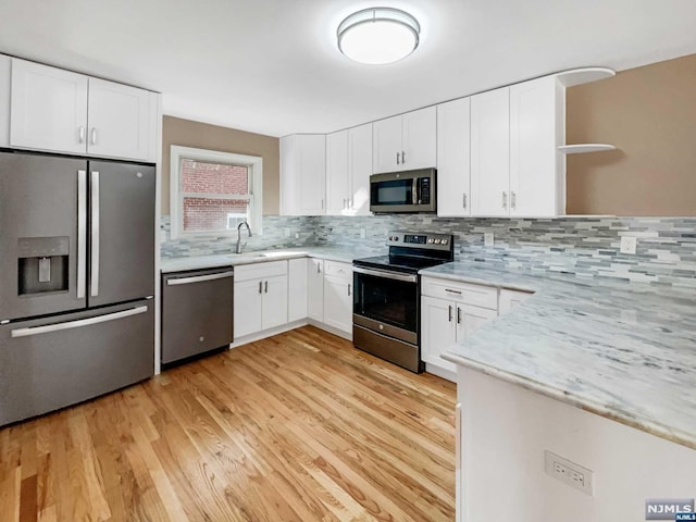 kitchen featuring stainless steel appliances, light stone counters, backsplash, white cabinets, and light wood-type flooring