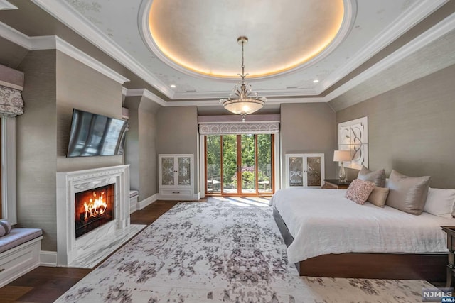 bedroom featuring dark hardwood / wood-style floors, a premium fireplace, crown molding, and a tray ceiling