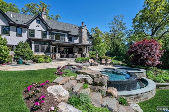 rear view of property with a patio area and an in ground hot tub