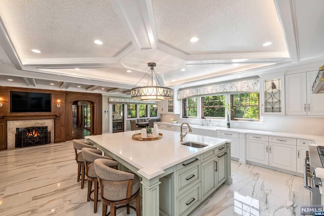 kitchen featuring a breakfast bar, a kitchen island with sink, sink, pendant lighting, and white cabinets