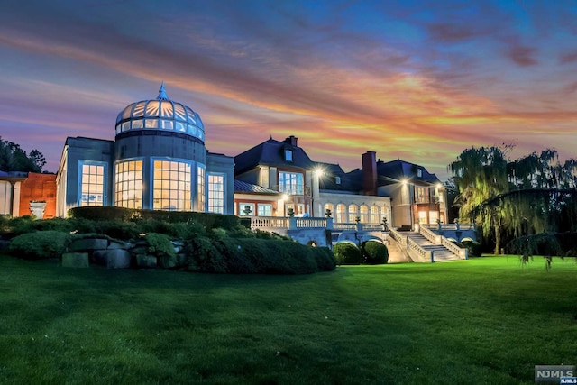 back house at dusk featuring a lawn