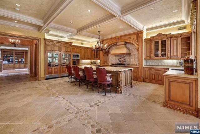 kitchen featuring coffered ceiling, beamed ceiling, an island with sink, pendant lighting, and custom exhaust hood