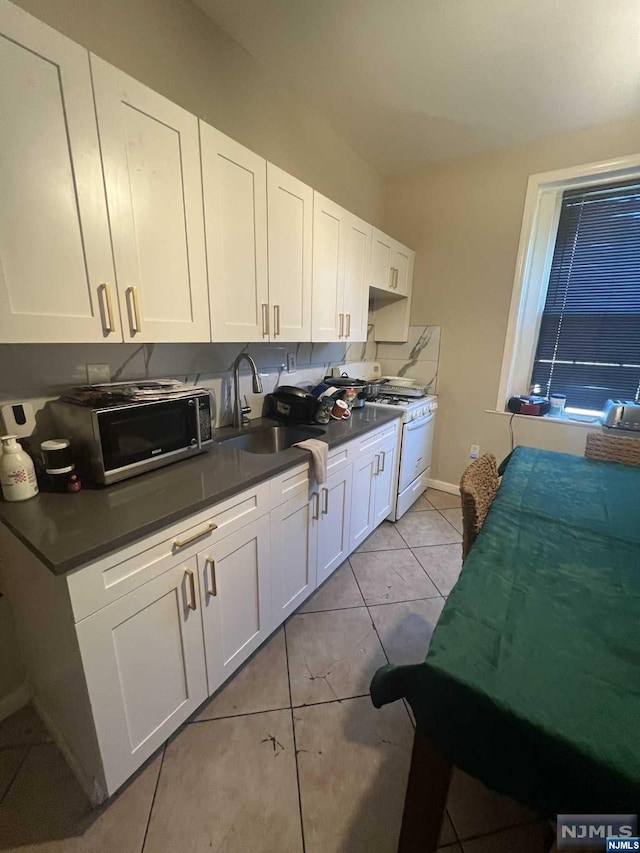 kitchen with white cabinets, light tile patterned floors, white range with gas cooktop, and sink