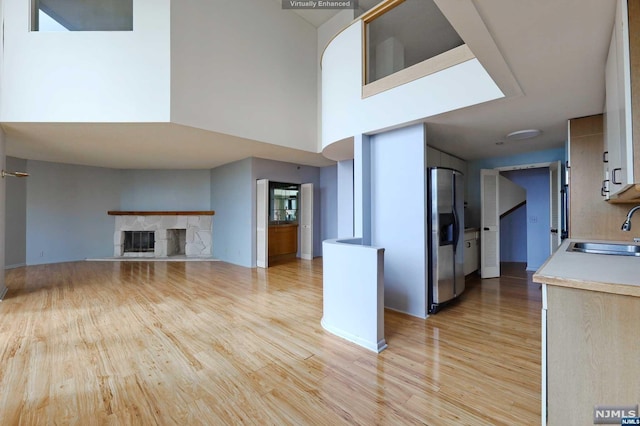 kitchen featuring stainless steel fridge, sink, light hardwood / wood-style flooring, a fireplace, and a high ceiling