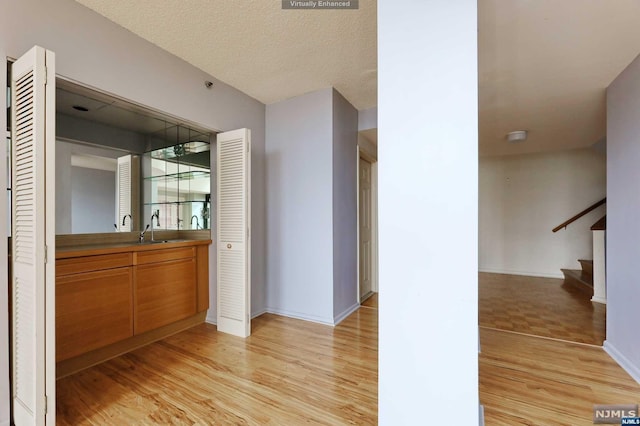 hall with a textured ceiling, sink, and light hardwood / wood-style flooring