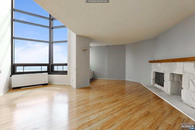 unfurnished living room featuring light hardwood / wood-style floors, a stone fireplace, a textured ceiling, and radiator