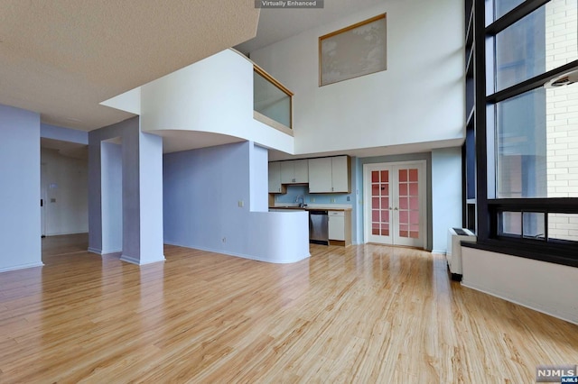 unfurnished living room with a textured ceiling, light hardwood / wood-style flooring, a high ceiling, and sink