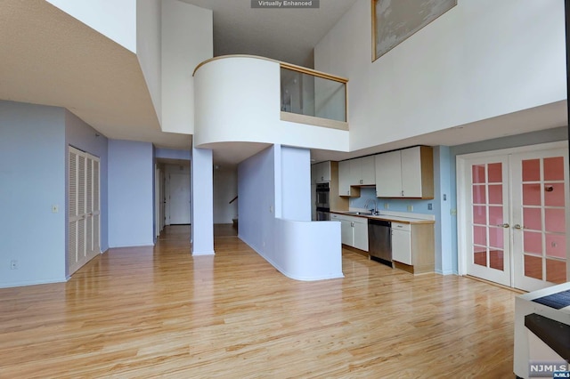 kitchen with white cabinetry, french doors, stainless steel appliances, a high ceiling, and light hardwood / wood-style flooring