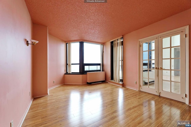 unfurnished room with light hardwood / wood-style floors, radiator heating unit, a textured ceiling, and french doors